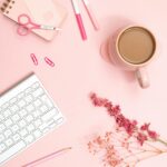 Aesthetic flat lay of a pink desk featuring stationery, coffee, and flowers for a modern workspace vibe.